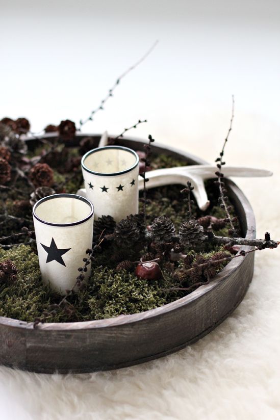 a Nordic fall centerpiece of a wooden tray with moss, pinecones, nuts, branches, antlers and candleholders with stars