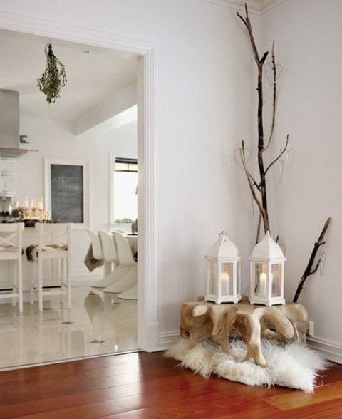 a Nordic decoration of a wooden slab table, a faux fur rug, branches and white candle lanterns