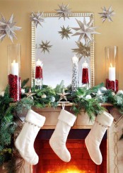 a gorgeous Christmas mantel with an evergreen and silver ornament garland, stars, candles and elegant white stockings with silver bells for a chic and refined space