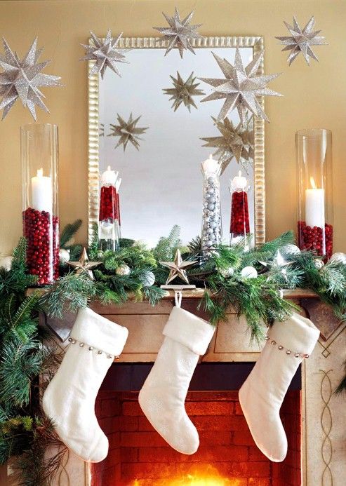 a gorgeous Christmas mantel with an evergreen and silver ornament garland, stars, candles and elegant white stockings with silver bells for a chic and refined space