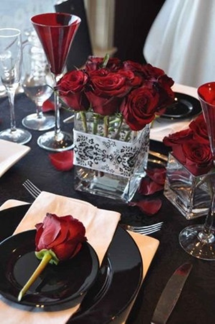 a bold red and black Halloween tablescape with plenty of red roses, burgundy goblets and some black plates is a very chic idea