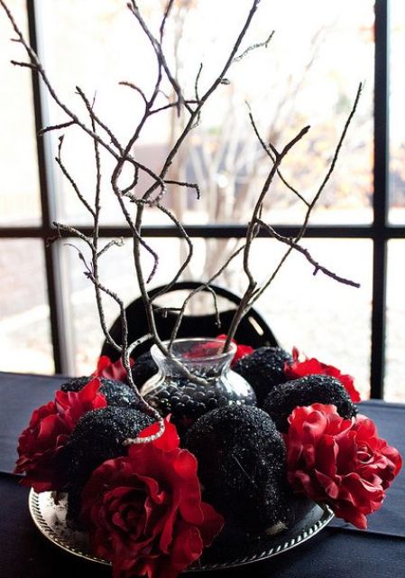 a refined red and black Halloween centerpiece of bold blooms and black glitter skulls plus branches in a vase in the center