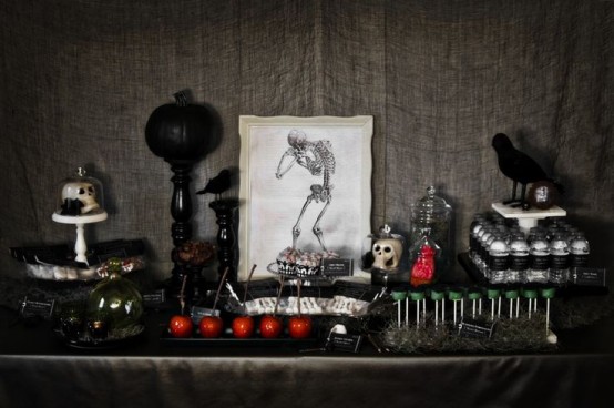 a vintage Halloween dessert table with candied apples, various desserts, a black pumpkin on a stand and a crow is chic and stylish
