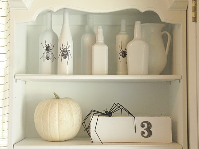 white Halloween decor with bottles with flies and spiders, a white pumpkin and more spiders is a very cool and stylish decor idea