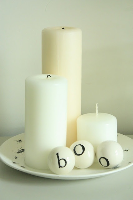 white pillar candles and white balls with letters compose a cool Halloween decoration in minimalist style