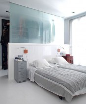 a neutral bedroom with a half wall and a frosted glass wall that divides the bedroom and walk-in closet in the space