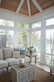 a beach sunroom with neutral furniture, a woven table, blooms and greenery and a cool beach view