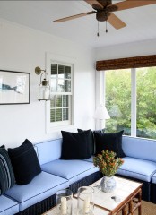 a modern beachy sunroom with a blue L-shaped sofa, black pillows, wooden tables and candles and art