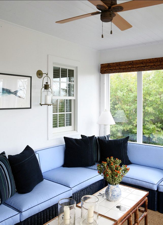 a modern beachy sunroom with a blue L shaped sofa, black pillows, wooden tables and candles and art