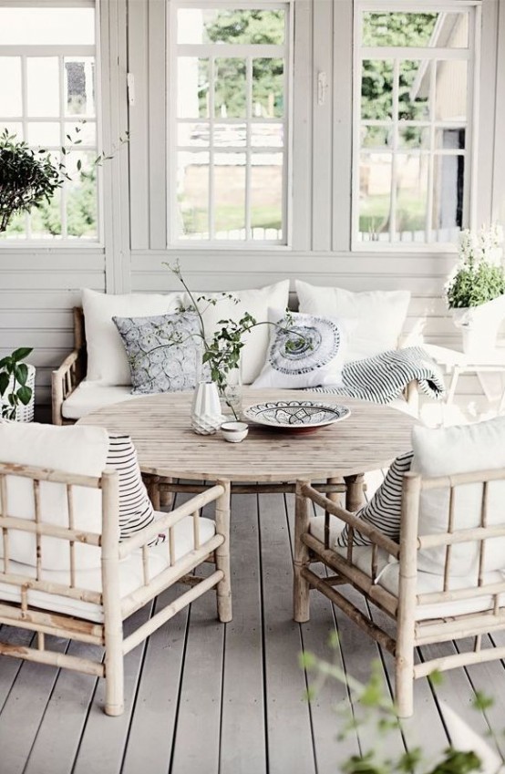 a coastal Nordic sunroom with simple wooden furniture, white and light blue pillows, greenery and elegant vases
