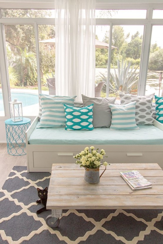 a beach farmhouse sunroom with neutral furniture with storage, a wooden table and light blue and mint blue pillows and upholstery