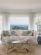 a beach sunroom with a modern neutral sofa, a driftwood and glass table and printed pillows and light green curtains