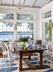 a vintage beach sunroom with a wooden table, blue and white printed chairs with covers, a rug and vintage chandeliers