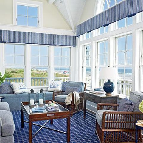 a nautical sunroom with a blue carpet, blue curtains, vintage wood furniture with blue upholstery and a gorgeous view