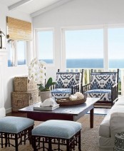 a vintage rustic coastal sunroom with dark wooden furniture with blue upholstery, baskets, shades and a white sofa plus a cool view
