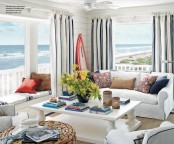 a modern beach sunroom with striped curtains, elegant white furniture, a woven ottoman and red touches