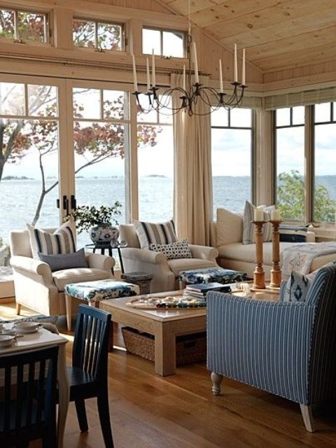 a coastal sunroom in rustic style with neutral and blue furniture, a wooden table with baskets and a vintage chandelier