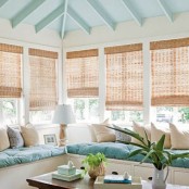a beach sunroom nook with a blue and neutral L-shaped bench and comfy cushions and pillows is lovely