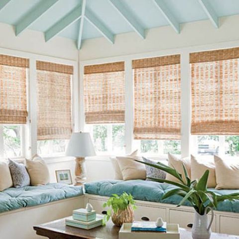 a beach sunroom nook with a blue and neutral L shaped bench and comfy cushions and pillows is lovely
