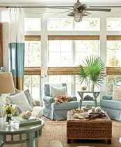 a coastal sunroom with neutral and light blue furniture, color block curtains, woven shades and a wicker table plus greenery