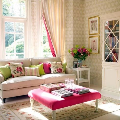 a bright and fun spring living room with printed wallpaper, colorful and floral pillows and curtains and a bold pink ottoman