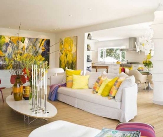 a bright spring living room with bold floral artworks, yellow printed pillows, oversized blooms in vases and pink pillows