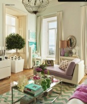 a refined living room in neutrals accented with green and purple touches, a crystal chandelier, a mirror and chevron patterns