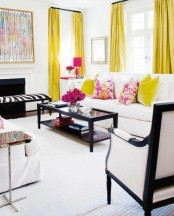 a monochromatic living room with bold yellow curtains, yellow and pink pillows, a pink lamp and blooms