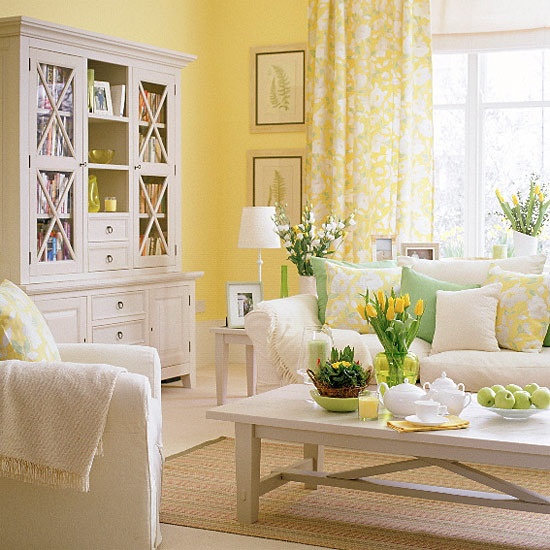 a colorful spring living room with yellow walls, neutral furniture, green and yellow pillows and blankets, yellow floral curtains, bright blooms and greenery