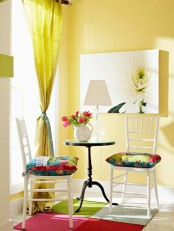 a bold living room with yellow walls, a yellow curtain, colorful pillows and artworks and a bright rug