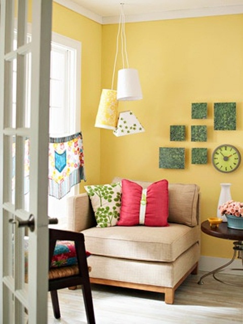 a bright living room with yellow walls, colorful pillows, pendant lamps, bold artworks and printed and bright textiles