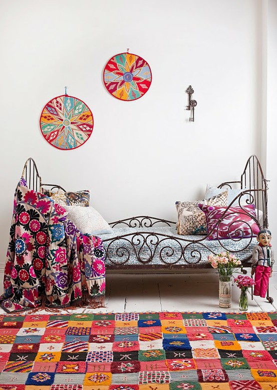 a neutral bedroom turned colorful and boho with a forged bed, printed bright bedding, a rug, pillows and even woven artwork on the wall