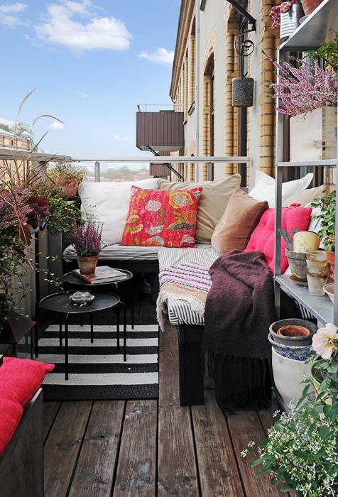a bold boho balcony with a striped corner sofa with colorful pillows, lots of potted greenery and blooms around feels relaxed and free spirited