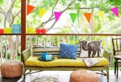 a super colorful balcony with a neon yellow loveseat, bold rugs and poufs, a colorful rug, colorful paper lanterns around