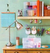 a colorful craft studio with mint green walls, an open shelf with books and various stuff, a metallic table lamp and emerald green decor is a lovely space to create in