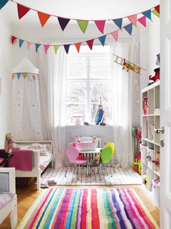 a neutral Scandinavian kids' bedroom made bright with super colorful textiles - rugs, bedding, buntings and a white storage unit with bright books and toys