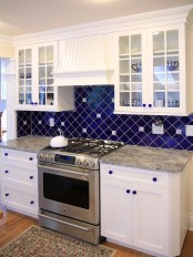 a wihte kitchen with shaker cabinets, grey countertops, a bold navy tile backsplash clad with a geometric pattern and matching glass knobs is a cool idea