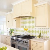 a vintage tan kitchen with a green and white geometric tile backsplash, with neutral countertops and green accessories to echo with the backsplash