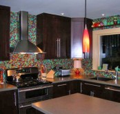 a dark-stained kitchen with grey stone countertops and a super colorful mosaic tile backsplash is a fun idea