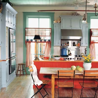 a bold vintage kitchen with green walls, a red kitchen island, a powder blue cabinet, stainless steel appliances and orange chairs