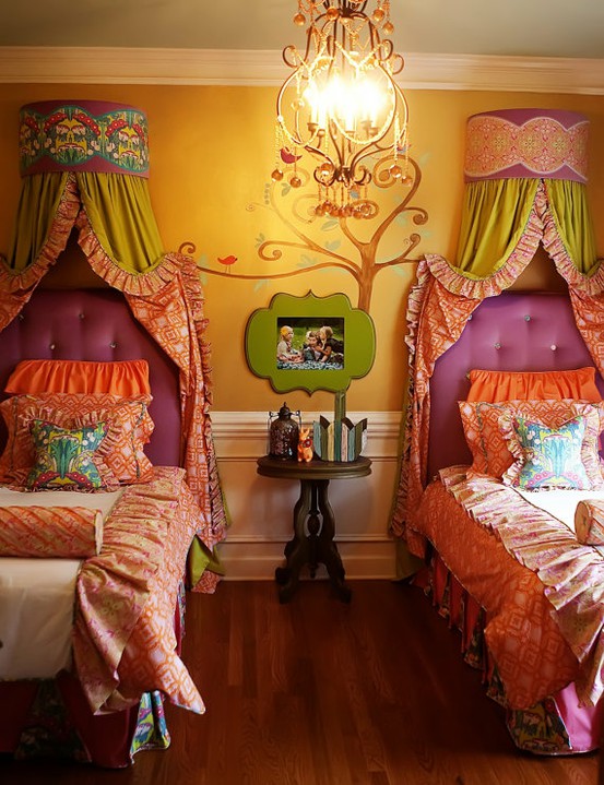 a colorful shared kids' room with a yellow and white wall with paneling, purple upholstered beds with bright bedding, colorful canopies of fabric and bright artwork