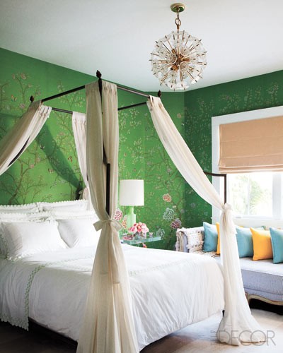an elegant bedroom with green printed wallpaper, a canopy bed with neutral curtains, a windowsill daybed with colorful pillows