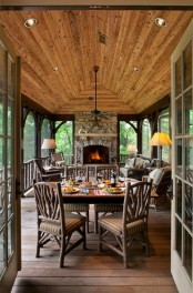 a rustic screened patio with a fireplace, wicker furniture with upholstery, a wooden table and chairs, some cozy textiles