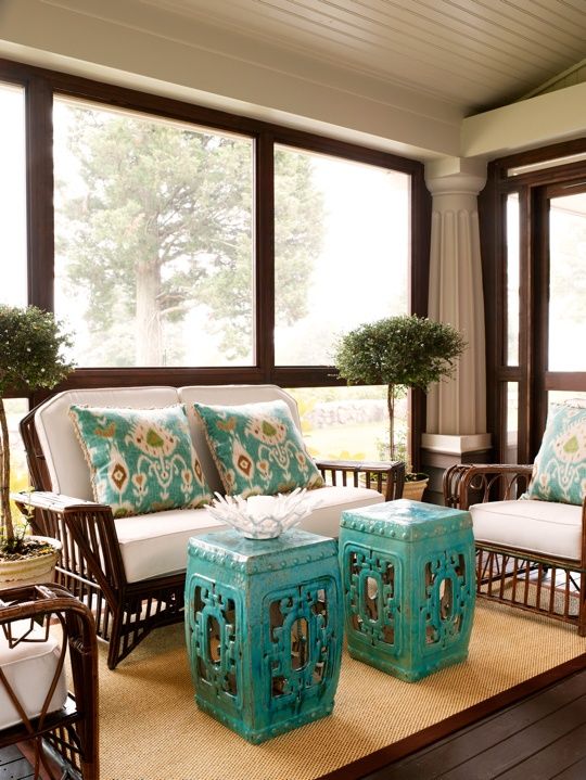 a bright colonial screened porch with dark stained furniture with white upholstery, turquoise pillows and side tables and potted plants