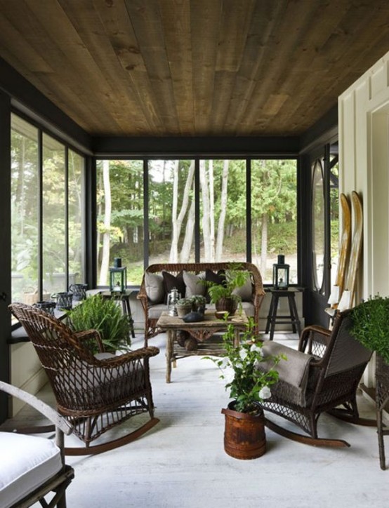 a farmhouse screened patio with dark wicker furniture, grey upholstery and pillows, potted greenery and lanterns