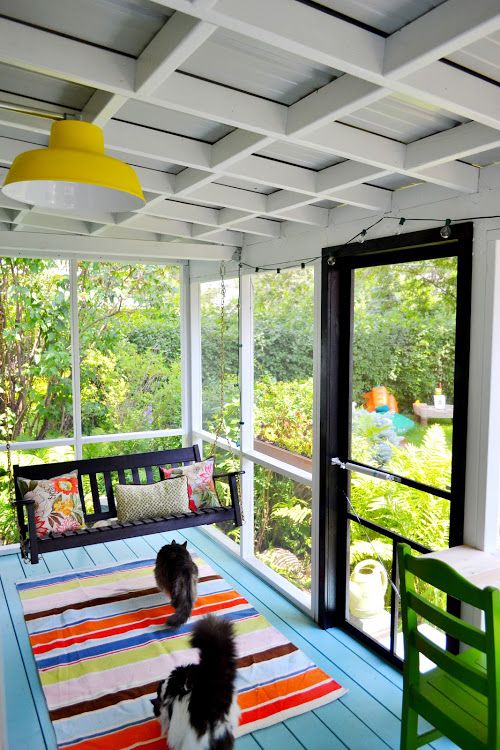 a colorful screened porch with a dark stained hanging bench, colorful rug and pillows and bright pendant lamps