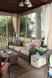 a cozy small screened porch with wicker furniture with neutral upholstery, a shabby chic chest, potted blooms and lanterns