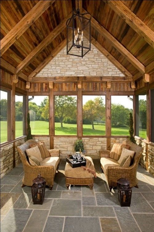 a chalet-styled screened porch with wicker furniture with beige upholstery, dark metal lanterns, greenery and a pendant lantern