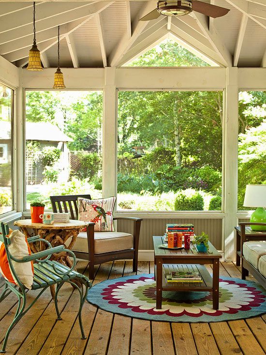 a colorful shabby chic screened porch with white upholstered furniture, a stained coffee table, a blue chair and a bold printed rug plus views