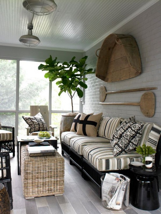 a rustic screneed porch with black furniture with striped upholstery, a side table and a wicker pouf, potted greenery and oars on the wall